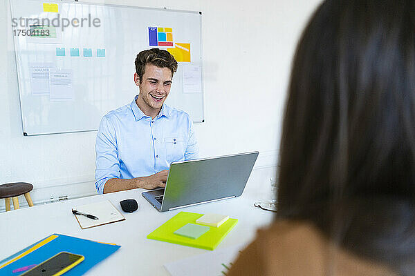 Lächelnder Geschäftsmann  der am Schreibtisch im Büro am Laptop arbeitet