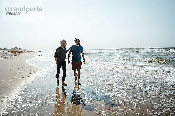 Vater und Sohn gehen gemeinsam im nassen Sand am Strand spazieren