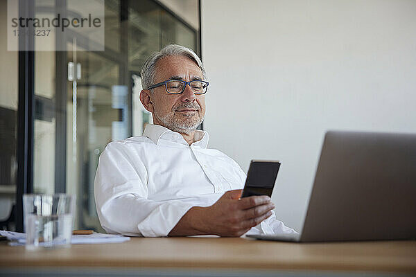 Lächelnder Geschäftsmann benutzt Mobiltelefon im Büro