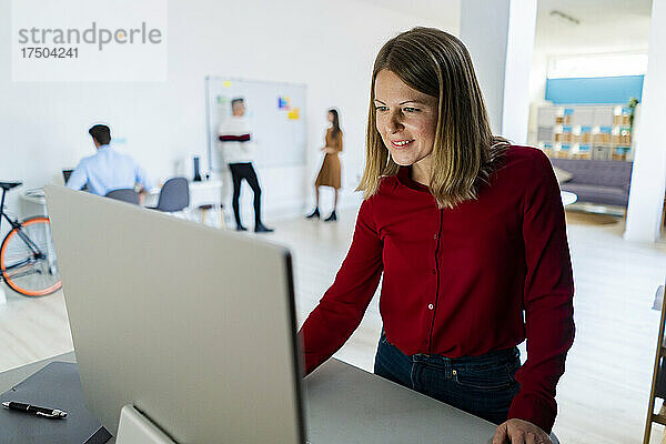 Geschäftsfrau mit blonden Haaren nutzt Desktop-PC im Büro
