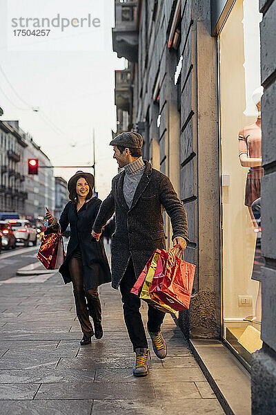 Fröhliches junges Paar spaziert gemeinsam mit Einkaufstüten durch die Stadt