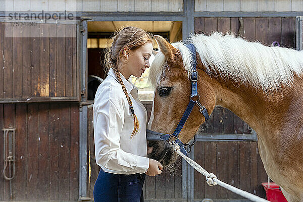 Junge Frau mit Pferd steht im Stall