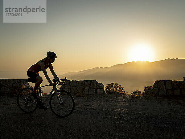 Sportlerin fährt bei Sonnenuntergang Mountainbike
