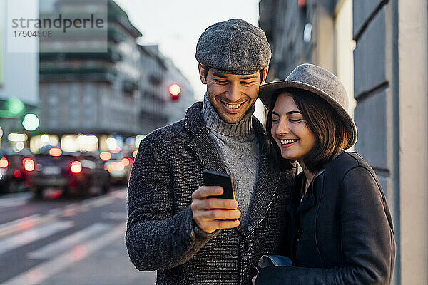 Glückliches Paar in warmer Kleidung  das Smartphone auf der Straße teilt