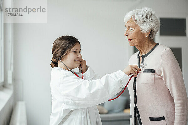 Enkelin mit Stethoskop untersucht Großmutter zu Hause
