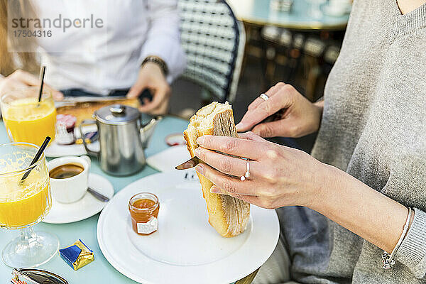 Junge Frau schneidet Baguette auf Teller im Café