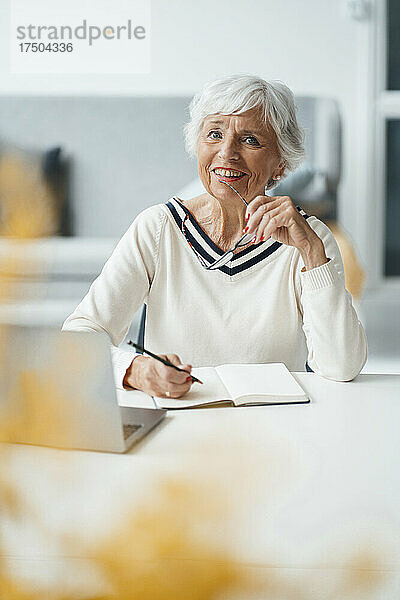 Ältere Frau hält Brille und Laptop am Tisch