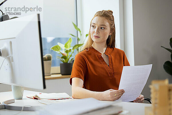 Geschäftsfrau mit Papier blickt im Büro auf den Computer