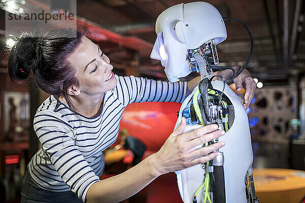 Lächelnder Techniker mit Arm um menschlichen Roboter in der Werkstatt
