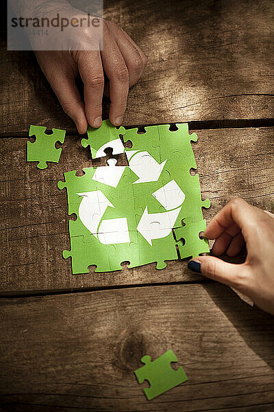 Freunde schließen sich dem Recycling-Symbol-Puzzle auf dem Tisch an