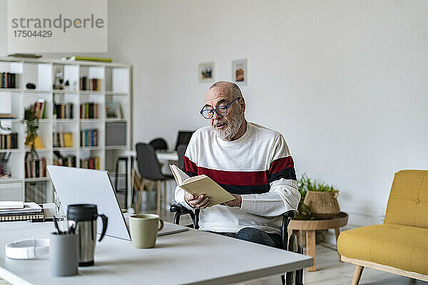 Älterer behinderter Mann liest Tagebuch im Heimbüro