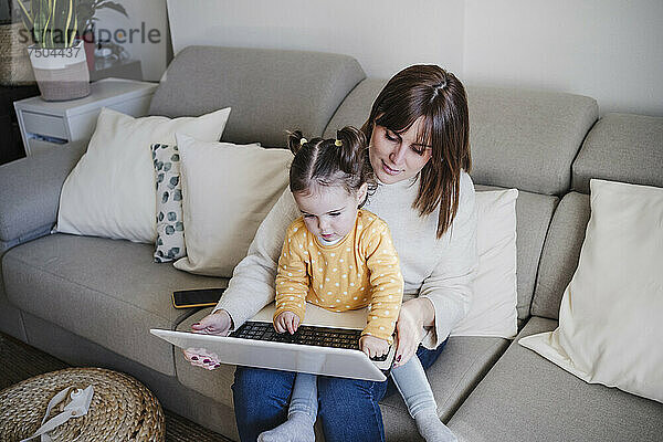 Mutter benutzt Laptop mit Tochter auf Sofa