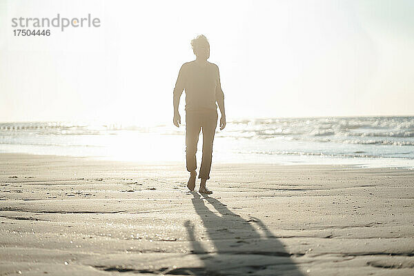 Älterer Mann geht an einem sonnigen Tag am Strand spazieren