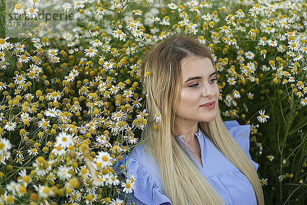 Blonde Frau betrachtet inmitten von Blumen auf einer Wiese