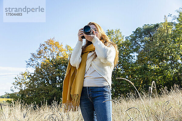 Junge Frau fotografiert mit der Kamera  während sie im Gras steht
