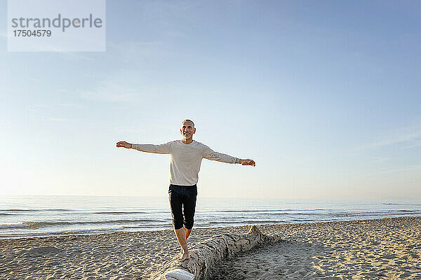 Mann balanciert auf Baumstamm am Strand