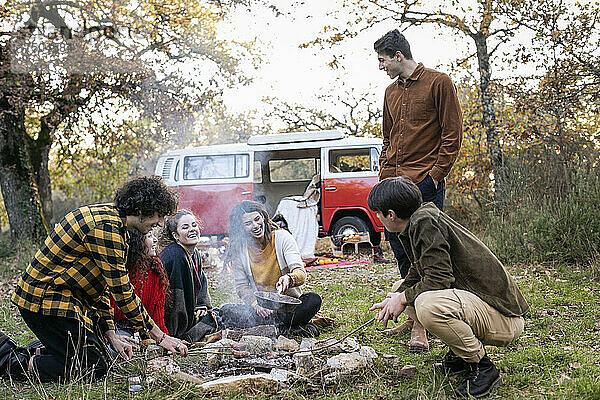 Fröhliche Freunde kochen Würstchen im Herbstwald beim Picknick