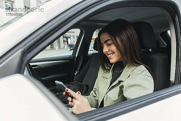 Lächelnde Frau benutzt Mobiltelefon im Auto