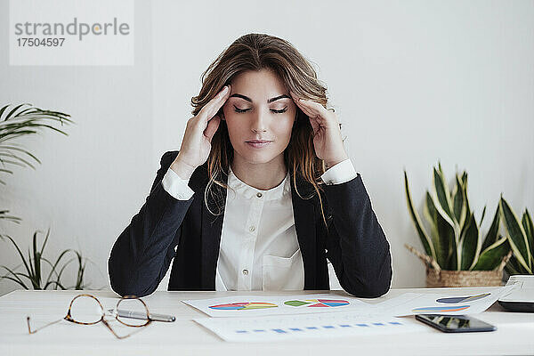 Müde Geschäftsfrau mit Kopf in den Händen sitzt am Schreibtisch im Büro