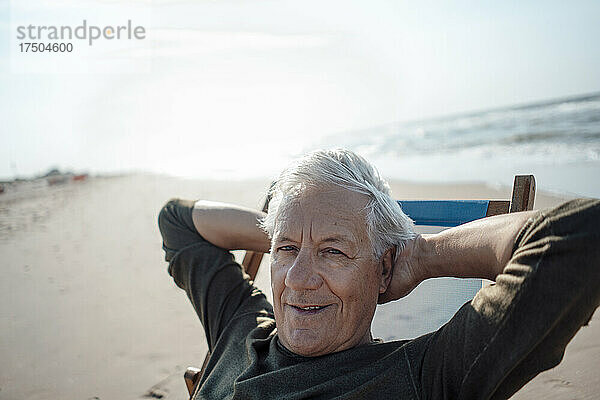 Lächelnder Mann entspannt sich auf einem Stuhl am Strand