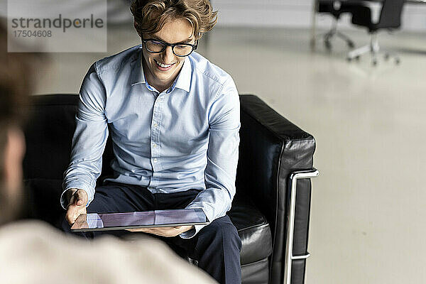 Lächelnder junger Geschäftsmann mit digitalem Tablet  der in der Lobby an einer Geschäftsstrategie arbeitet