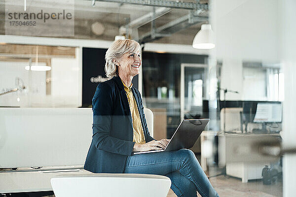 Lächelnde Geschäftsfrau mit Laptop auf dem Schreibtisch
