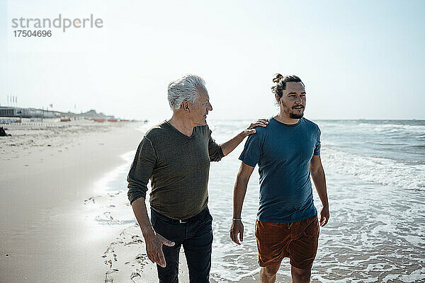 Älterer Mann spricht am Strand mit seinem Sohn  die Hand auf der Schulter