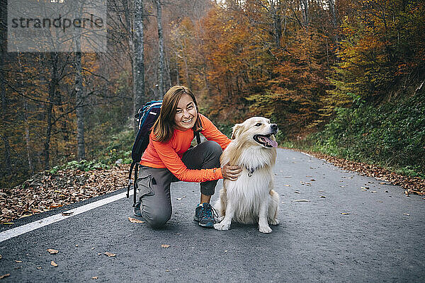 Lächelnde Frau kniet mit Hund auf der Straße