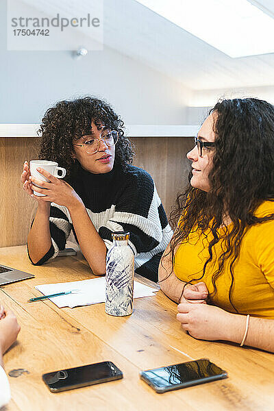 Geschäftsfrau mit Kaffeetasse diskutiert mit Kollegen im Büro