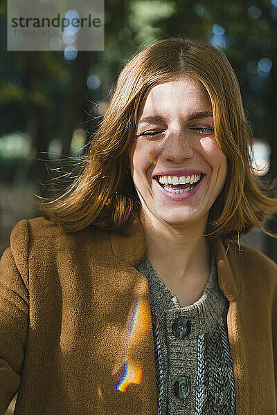 Junge Frau mit geschlossenen Augen lacht im Herbstpark