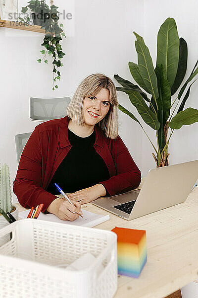 Junge Geschäftsfrau mit Tagebuch sitzt am Schreibtisch im Kreativbüro