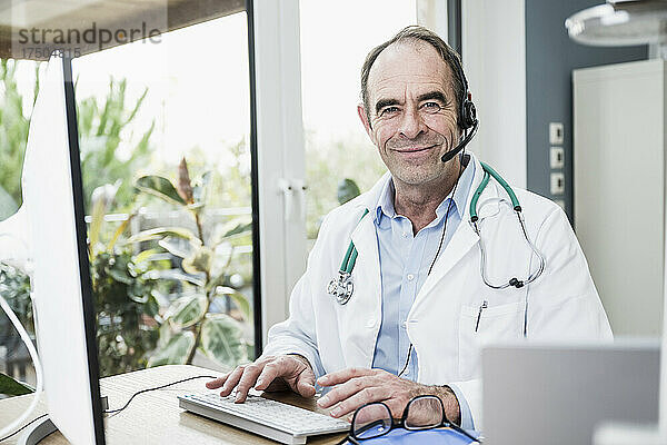 Lächelnder Arzt mit Headset sitzt in der Klinik