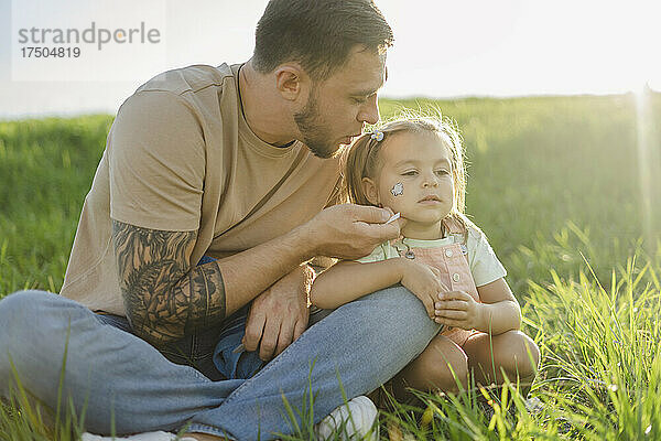 Vater tätowiert Tochter im Gesicht  sitzt im Gras