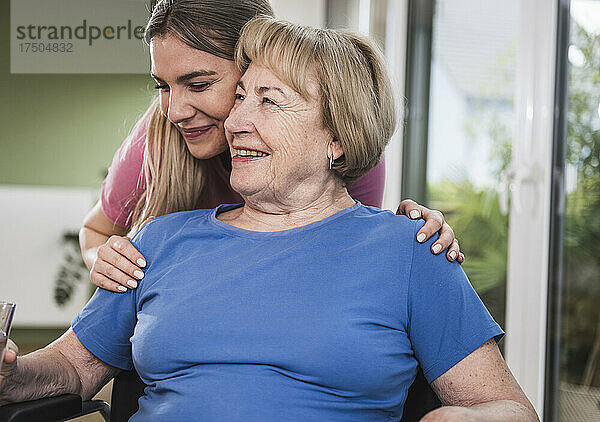 Krankenschwester umarmt behinderte ältere Frau von hinten zu Hause