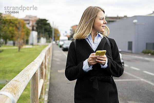 Blonde Frau hält Smartphone auf der Straße
