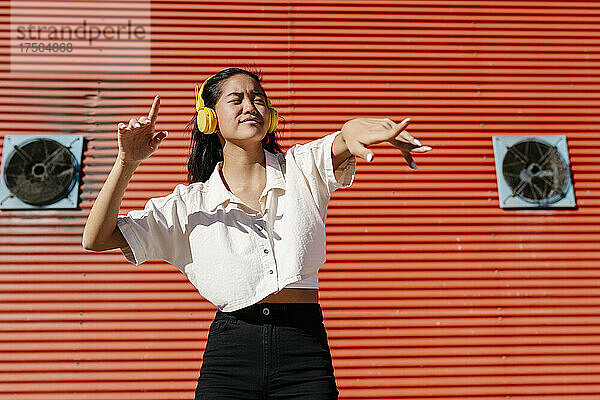 Junge Frau mit Kopfhörern tanzt an einem sonnigen Tag