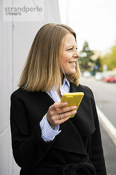 Lächelnde Frau hält Smartphone an der Wand
