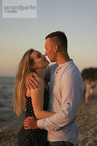 Zärtliches Paar umarmt sich bei Sonnenuntergang am Strand