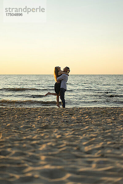 Mann hebt Frau am Strand bei Sonnenuntergang