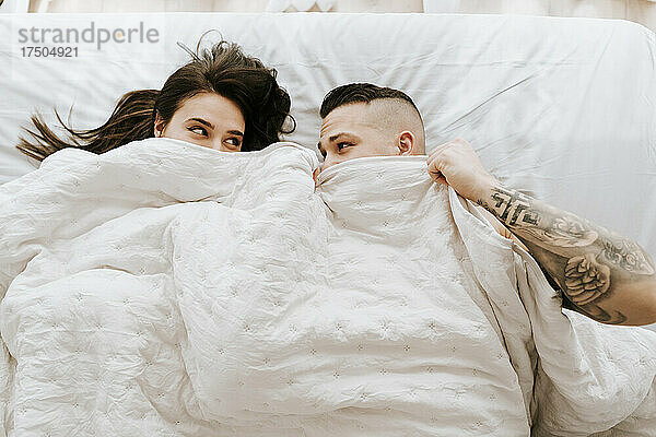 Paar schaut sich unter der Bettdecke im Bett an