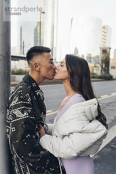 Romantische Frau küsst ihren Freund  der sich in der Stadt an eine Stange lehnt