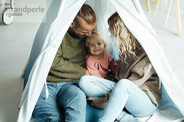 Verspielte Tochter sitzt mit Eltern im Zelt zu Hause