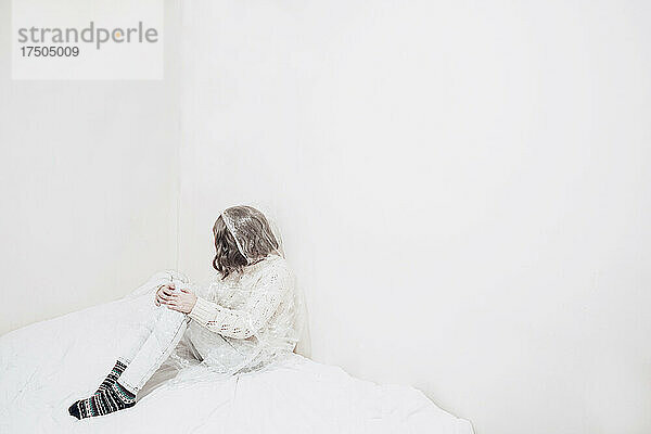 Traurige Frau  in Plastik gehüllt  sitzt an der Wand auf einer Bettdecke