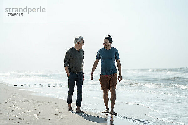 Älterer Mann mit der Hand in der Tasche geht mit seinem Sohn am Strand spazieren