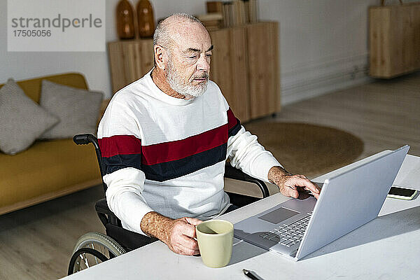 Behinderter Geschäftsmann mit Kaffeetasse und Laptop im Heimbüro