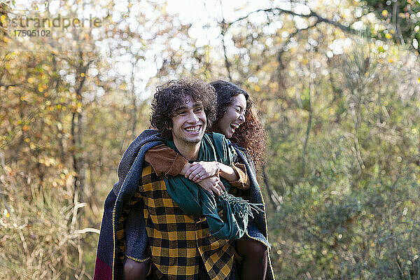 Fröhlicher Mann gibt seiner Freundin Huckepack und lacht im Herbstwald