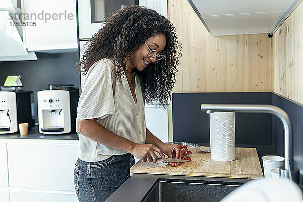 Lächelnde Geschäftsfrau mit lockigem Haar schneidet Kirschtomaten in der Küche der Büro-Cafeteria