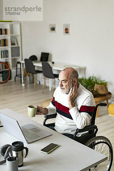 Leitender Freiberufler im Rollstuhl hält Kaffeetasse im Heimbüro
