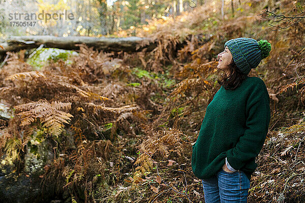Lächelnde Frau mit der Hand in der Tasche  die in den Wald blickt