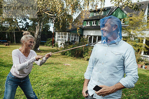 Verspielte Frau legt einem Mann im Hinterhof ein Schmetterlingsfischernetz ins Gesicht